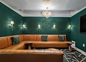 Thumbnail 17 of 43 - A brown leather couch with green pillows in front of a green wall with a chandelier at The Carousel Apartments, Richmond, Virginia