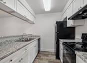 Thumbnail 11 of 26 - A kitchen with a black refrigerator and white cabinets.