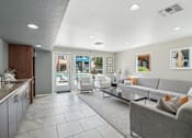 Thumbnail 19 of 26 - A modern living room with a grey couch and a kitchen area with a sink.