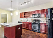 Thumbnail 18 of 22 - A kitchen with red cabinets and black appliances at Overlook at Stone Oak Park Apartments, San Antonio