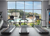 Thumbnail 17 of 48 - a gym with cardio equipment and a window view of a swimming pool