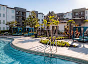 Thumbnail 29 of 60 - Pool deck with cabanas and palm tree landscaping at Avli At Crosstown Center Apartments, Florida