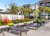 Thumbnail 6 of 60 - Property entrance sign with lounge chairs and landscaping at Avli At Crosstown Center Apartments, Florida