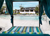 Thumbnail 7 of 60 - Poolside cabana with striped cushions and teal curtains at Avli At Crosstown Center Apartments, Florida, 33619