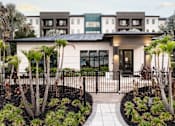 Thumbnail 4 of 60 - Clubhouse building with paver walkway and tropical landscaping at Avli At Crosstown Center Apartments, TAMPA, FL