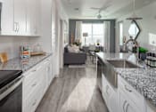 Thumbnail 8 of 60 - Galley kitchen with white cabinets and granite countertops at Avli At Crosstown Center Apartments, TAMPA, FL 33619