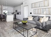 Thumbnail 9 of 60 - Open concept living room with gray sofa and kitchen at Avli At Crosstown Center Apartments, TAMPA