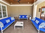 Thumbnail 25 of 54 - Three cushioned benches and a small table under a ceiling fan on the outdoor covered clubhouse patio
