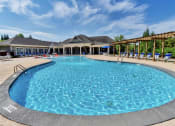 Thumbnail 21 of 54 - Sparkling pool with fountains, and lounge chairs under a wooden pergola near a clubhouse