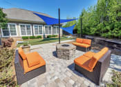 Thumbnail 23 of 54 - Outdoor cushioned chairs surrounding a fire pit on a cobblestone patio with a shaded grassy area