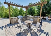 Thumbnail 42 of 54 - Grilling station with small wooden pergola, outdoor bar, and tables with chairs near trees