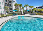 Thumbnail 29 of 32 - a swimming pool with blue lounge chairs and umbrellas in front of an apartment building