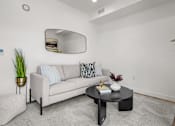 Thumbnail 31 of 36 - A living room with a grey couch, a round mirror, a coffee table, and a potted plant.