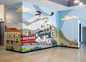 Thumbnail 8 of 36 - A train is on a wall mural with clouds and a plane.