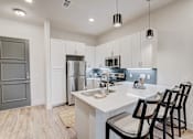 Thumbnail 17 of 23 - Modern kitchen with island seating and white cabinetry at The Mill Old Town Apartments, Lewisville, TX 75057