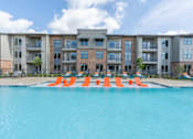 Thumbnail 12 of 35 - a swimming pool with orange lounge chairs in front of an apartment building at One Preston Station, Celina, TX, 75009