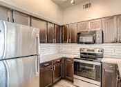 Thumbnail 5 of 20 - A kitchen with a stainless steel refrigerator, microwave, oven, and cabinets with quartz countertops.