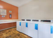 Thumbnail 11 of 29 - four washers and dryers in a laundry room with orange walls and wooden floors