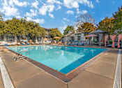 Thumbnail 4 of 30 - A large outdoor swimming pool surrounded by trees and umbrellas.