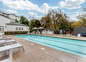 Thumbnail 2 of 33 - A swimming pool surrounded by lounge chairs and a white building.