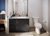 Thumbnail 4 of 25 - A bathroom with a white toilet, a sink with a mirror above it, and a cabinet below the mirror.
