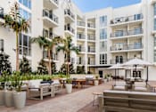Thumbnail 4 of 28 - A white apartment building with a patio area in front.