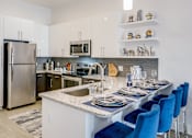 Thumbnail 5 of 33 - a kitchen with white cabinets and a large island with a granite countertop and blue chairs  at Link Apartments® Mixson, South Carolina
