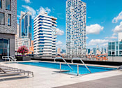 Thumbnail 10 of 34 - A swimming pool on a rooftop with a city skyline in the background.