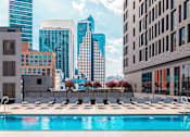 Thumbnail 9 of 34 - A swimming pool with sun loungers in the foreground and a city skyline in the background.