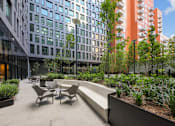 Thumbnail 33 of 39 - A patio with chairs and a bench is surrounded by plants and trees at Link Apartments® QPN, Long Island City, New York