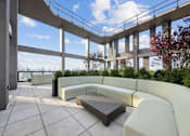 Thumbnail 25 of 39 - A patio with a bench and a table with a railing and trees in the background at Link Apartments® QPN, Long Island City, New York