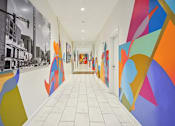 Thumbnail 26 of 32 - a hallway with colorful paintings on the walls and a white tile floor at Link Apartments® 4th Street, North Carolina, 27101