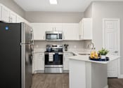 Thumbnail 1 of 23 - A kitchen with a black fridge, white cabinets, and a white island.