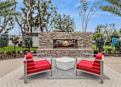 Thumbnail 13 of 17 - A patio with a stone fireplace, two red chairs and a white table.