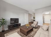 Thumbnail 4 of 27 - A living room with a white couch, a wooden coffee table, a flat screen TV, and a potted plant.