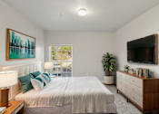 Thumbnail 3 of 20 - A bedroom with a bed, nightstand, and a painting on the wall.