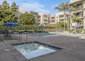 Thumbnail 16 of 28 - a swimming pool with chairs and umbrellas in front of an apartment building