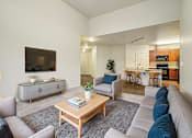 Thumbnail 4 of 19 - A living room with a grey couch, a wooden coffee table, and a television on the wall.