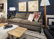 Thumbnail 4 of 21 - A living room with a grey couch, a wooden coffee table, and a lamp.