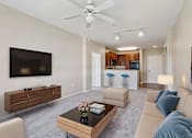 Thumbnail 2 of 25 - A living room with a brown coffee table and a flat screen TV mounted on the wall.