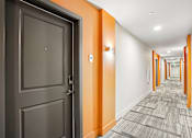 Thumbnail 9 of 31 - A hallway with orange walls and a grey door.