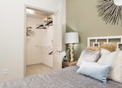 Thumbnail 6 of 21 - A bedroom with a bed, lamp, and a closet with clothes hanging.