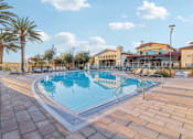 Thumbnail 15 of 38 - A large outdoor swimming pool surrounded by palm trees and a building in the background.