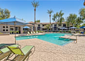 Thumbnail 25 of 28 - A pool surrounded by chairs and umbrellas with a building in the background.
