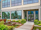 Thumbnail 25 of 31 - A modern building with a glass facade and a wooden walkway leading to the entrance.
