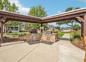 Thumbnail 13 of 31 - A wooden pergola over a concrete walkway with stone pillars.