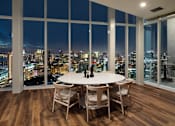 Thumbnail 13 of 33 - A dining table with chairs in front of a window overlooking a cityscape at night.