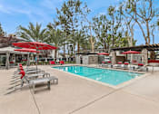 Thumbnail 8 of 17 - A pool area with red umbrellas and lounge chairs.