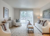 Thumbnail 9 of 14 - A living room with a white couch, a coffee table, and a window with a view of trees.