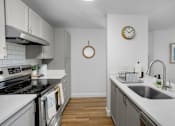 Thumbnail 7 of 27 - A kitchen with a stove, sink, and clock on the wall.